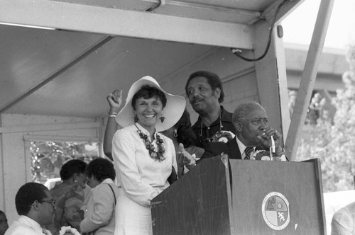 Pat Russell and Gilbert Lindsay speaking at a lectern during the 16th annual Easter parade, South Central Los Angeles, 1984