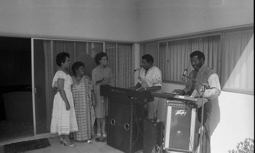 Three African American women watching musicians perform on a patio, Los Angeles, 1984