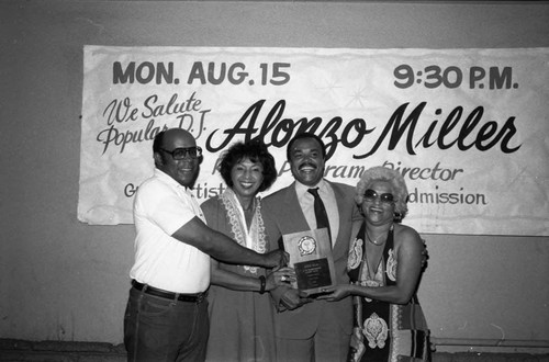 Alonzo Miller holding an award while posing with others at the Pied Piper nightclub, Los Angeles, 1983