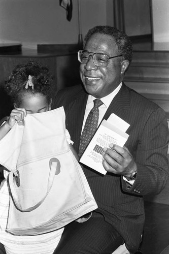 Alex Haley holding a copy of his book while sitting with a toddler, Los Angeles, 1981