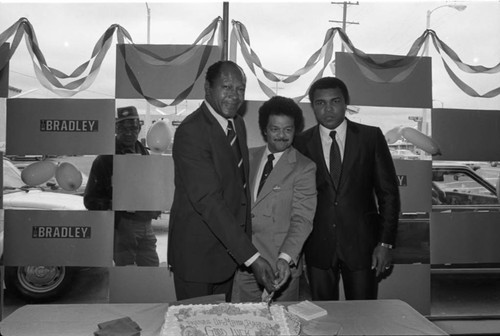 Tom Bradley, Bob Farrell, and Muhammad Ali posing while cutting a cake, Los Angeles, 1981