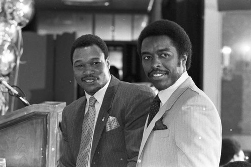 Larry Holmes and Jim Hill posing together at a press conference for the "Crown Affair" boxing event, Los Angeles, 1983