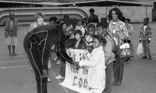 Michael Cooper shaking hands with a young girl on a playground, Los Angeles, 1985