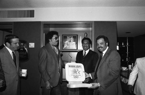 August Busch, III and others displaying a 1964 Olympics seat cushion, Los Angeles, 1982