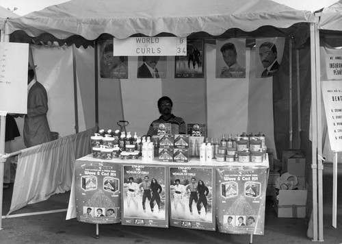 Black Agenda Business Fair participant standing in their booth, Los Angeles, 1983