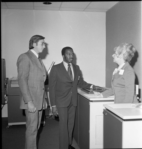 Two men in business suits talking with a woman in an office, Los Angeles, ca. 1973