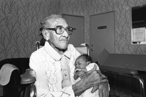 Mamie Smoot holding an infant while celebrating her 100th birthday, Los Angeles, 1983