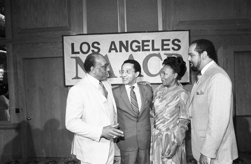 Bishop H. H. Brookins, Tony Brown, Maxine Waters and John T. McDonald III, talking together at a luncheon, Los Angeles, 1984