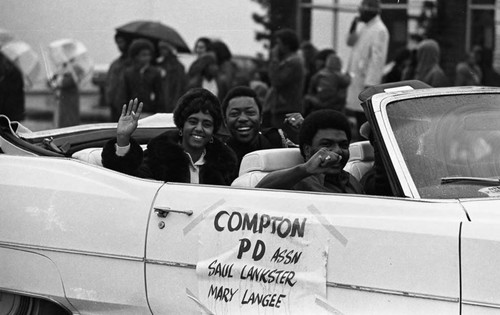 Mary Langee and Saul Lankster waving from a convertible during the Compton Christmas Parade, Compton, 1973