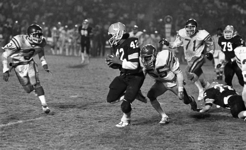 Crenshaw and Carson High School football teams running a play during a city championship game, Los Angeles, 1982