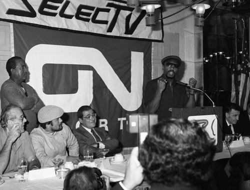 Marvin Hagler speaking from a lectern at the Los Angeles Athletic Club as Roberto Durán listens, Los Angeles, 1983