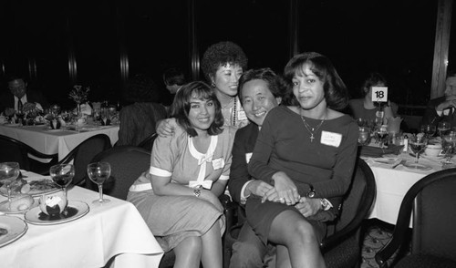 Three women and a man posing together around a dinner table, Los Angeles, 1989