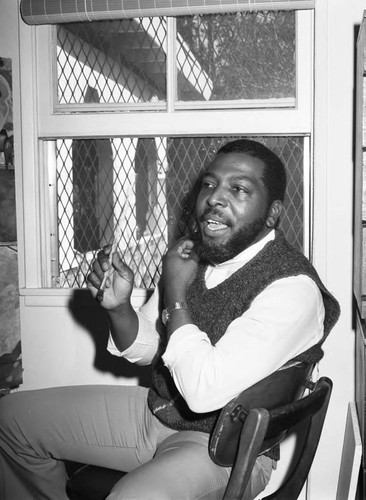 Ernest Johnson talking while sitting in front of a painting, Los Angeles, 1983