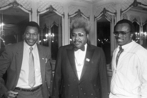 Don King standing with Larry Holmes and Michael Dokes at a press conference for the "Crown Affair" boxing event, Los Angeles, 1983