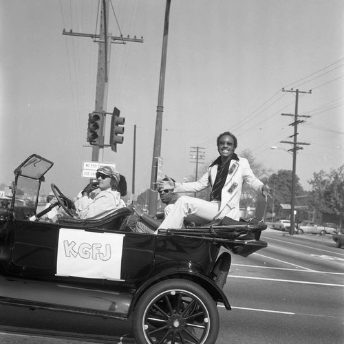 Watts Christmas Parade participants representing KGFJ riding in an antique automobile, Los Angeles, 1975