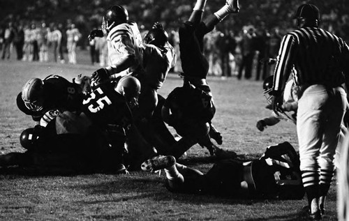 Crenshaw and Carson High School football teams running a play during a city championship game, Los Angeles, 1982