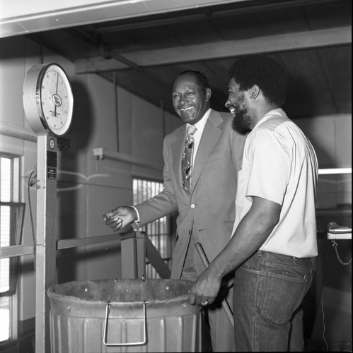 Tom Bradley stands with an Reynolds Aluminum Recycling employee near an industrial scale, Los Angeles, 1976