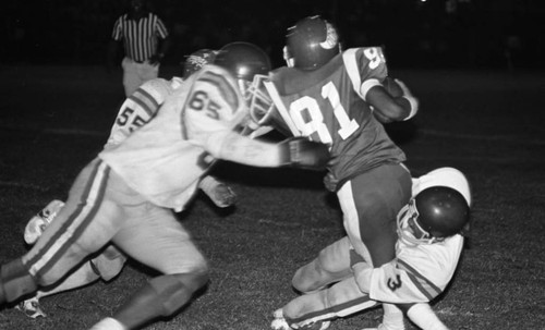 Crenshaw and Dorsey High School football teams running a play during a game, Los Angeles, 1982