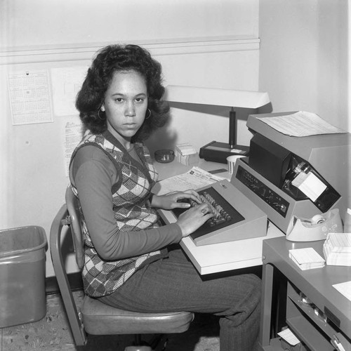 Keypunch operator posing at the keypunch machine at Compton College, Compton, 1972