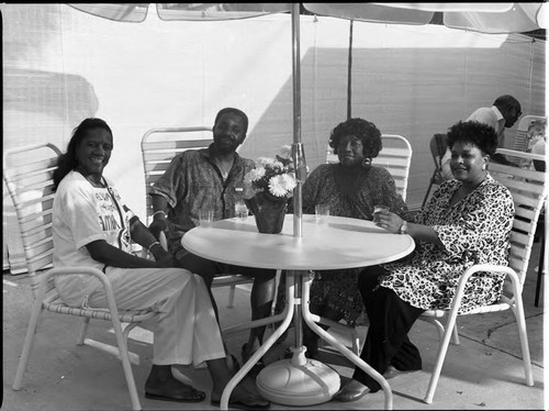 Three African American women and an African American man posing under a patio umbrella, Los Angeles, 1988