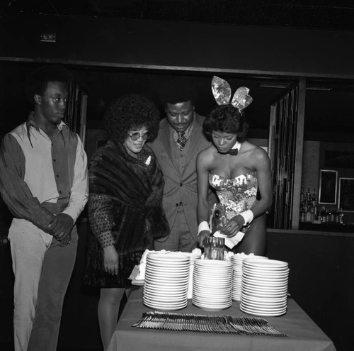 Woman in a Playboy bunny costume serving cake at a buffet, Los Angeles, 1972