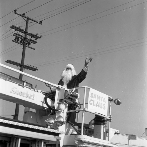 Watts Christmas parade participant Santa Claus waving from a fire truck, Los Angeles, 1975