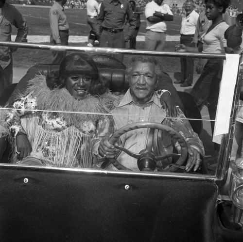 Flip Wilson and Redd Foxx sitting in an antique car during the Urban League's Celebrity All-Star Freedom Classic pre-game, Los Angeles, 1973