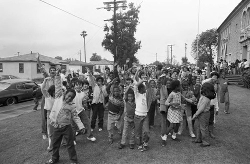 Ritter Elementary School children waving and pointing toward the sky, Watts (Los Angeles, Calif.), 1983