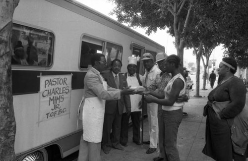 Rev. Charles Mims, Jr. handing a meal to a homeless woman, Los Angeles, 1986