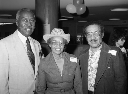 Nate Holden posing with Mary and Wilson Valley at Family Savings & Loan, Los Angeles, 1983