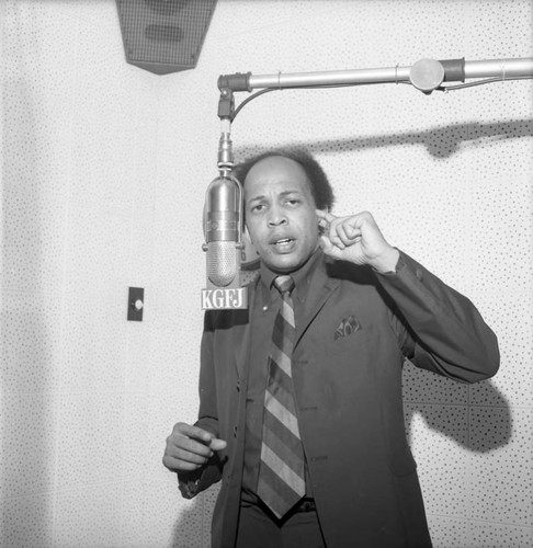 Booker Griffin standing at a microphone during a broadcast at KGFJ, Los Angeles, 1971