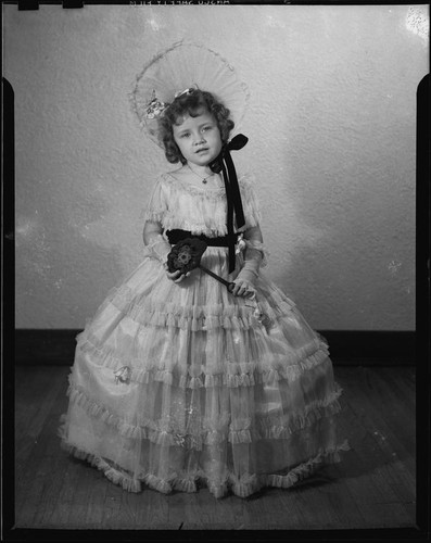 Helena Burnett in dress and bonnet holding a toy flower, 1947-1950