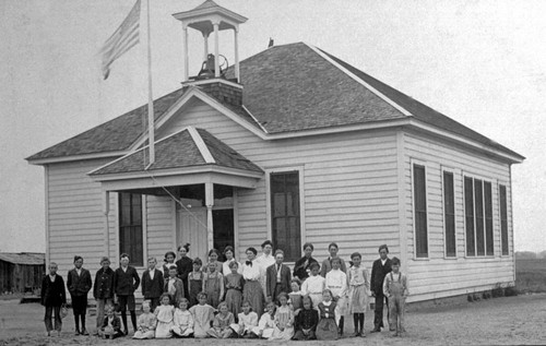 Students and teachers in front of schoolhouse