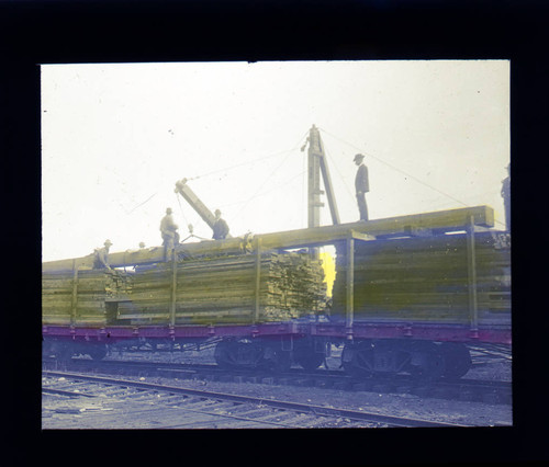 Men loading lumber on train, hand colored lantern slide