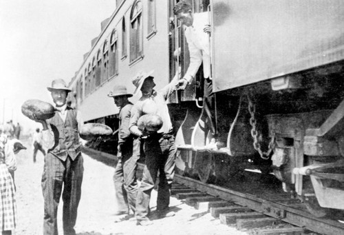 Men holding watermelons next to train