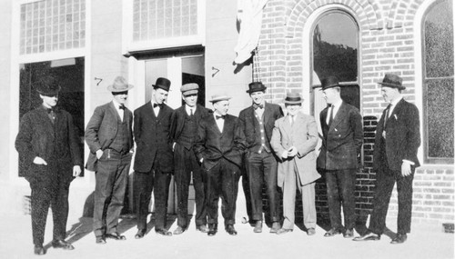 Men in suits posed in front of brick building