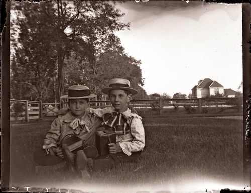 Harry and Friend seated in grass with school books, straw hats