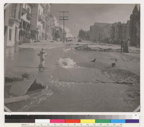 A ruptured water main gushes as fire rages in the distance. [Van Ness Ave. at Vallejo]