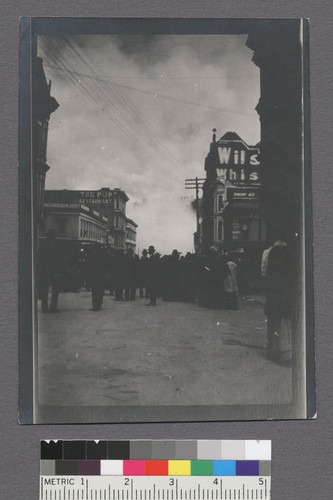 [Street scene showing crowd gathering with fire burning in distance. The Pup restaurant, left.]