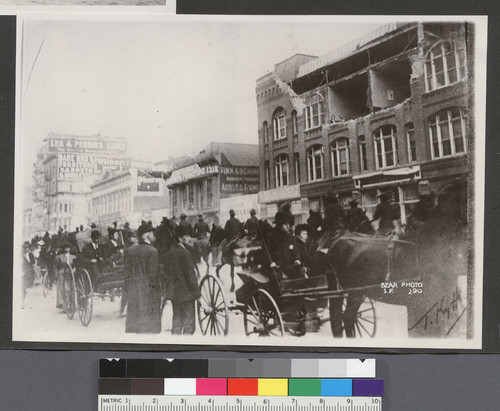 [Street scene of procession of soldiers. Earthquake-damaged building at right.]