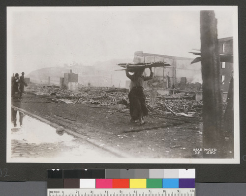 [Woman gathering roofing tin among ruins.]