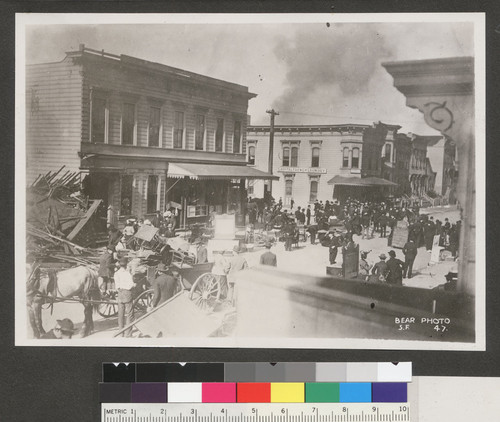 [Street scene of refugees with belongings during fire.]