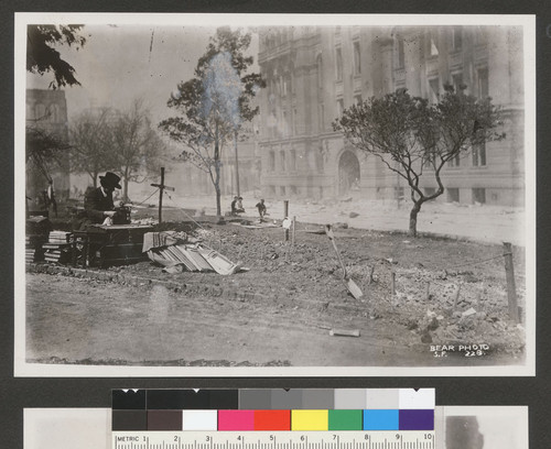 [Author Henry Lafler at typewriter next to fresh graves. Portsmouth Square. Hall of Justice in background, right.]