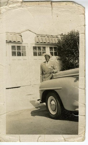 African American man in driveway, leaning against car