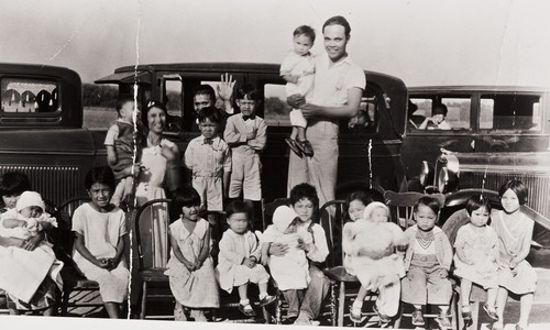 Christening party for Adeline Cabreana : Guadalupe Produce Labor Camp, Lompoc : 1932 ; the house Adeline and her brother Ernie were born in still stands, but is old and unoccupied ; back row L-R: Margaret Bautista, two unidentified, Irineo Cabreana holding son Ernie ; seated L-R: Nellie Abenido, Aurelia "Iree" Abenido, Visitacion "Viz" Abenido, five unidentified, Rudy Pili, Pastoria Deparini and Euphrasia Deparini