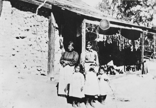 Margarita Bernal, Rosa Cota and children in front of Margarita's adobe house at Zanja de Cota : beef jerky is drying in the background : 1890s