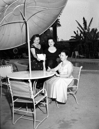 Women pose next to a pool