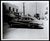 Charlotta Bass in the back seat of a car in front of Hooper Market, 1950-1952