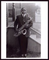 Paul Howard holding his saxophone at the front steps of a house, 1920s