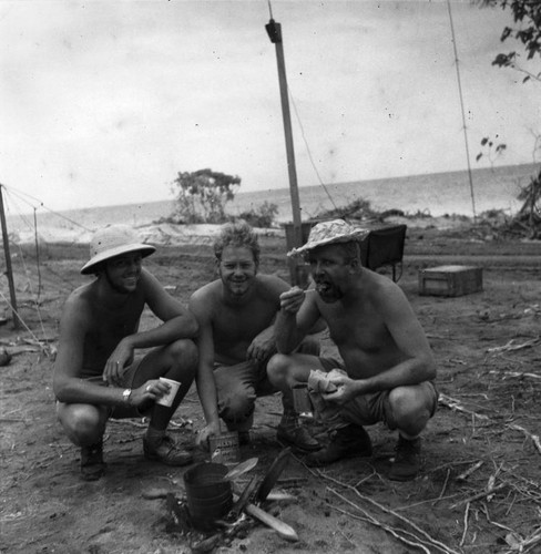 Crew members (left to right): Edward (Edward Sheldon) Barr, Bernard Darsey and Jeff (Norman J.) Holter enjoy a gourmet meal from cans "Abstain I" encampment on Eniman Island, Bikini Atoll, during the Capricorn Expedition (1952-1953). October 27, 1952